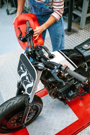 Mechanic woman with jerry can filling fuel tank of motorcycle on factory