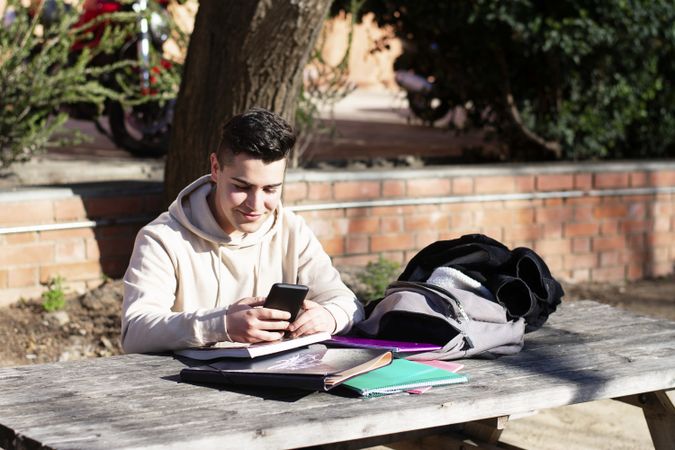 Young student sitting in a park while using a mobile phone on a wooden table
