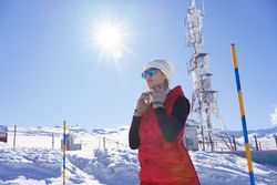 Low angle of focused female in warm clothes and sunglasses putting on headphones on snowy terrain