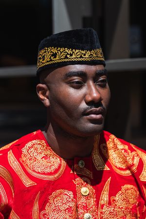 Thoughtful Black man in traditional clothes and headdress near building