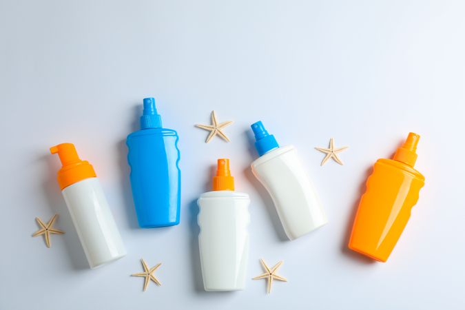 Flat lay composition with sunscreen sprays and starfishes on plain background, space for text. Summer vacation backdrop