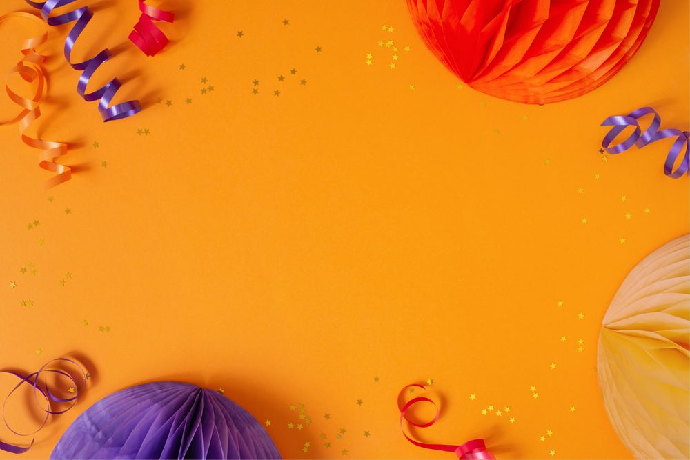 Paper lanterns, glitter and ribbon on orange background