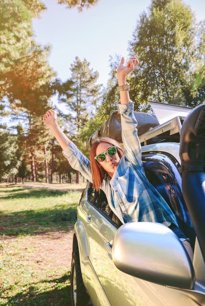Happy woman raising arms through the window car