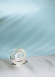 Internet “at” symbol with palm leaf shadow in blue room, vertical