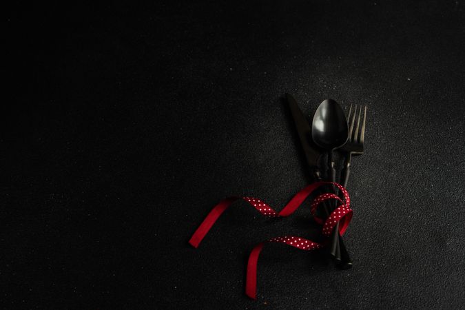 Dark cutlery on dark background tied with festive red ribbon with copy space