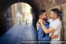 Two men facing each other in an embrace under a city bridge 42Vd34