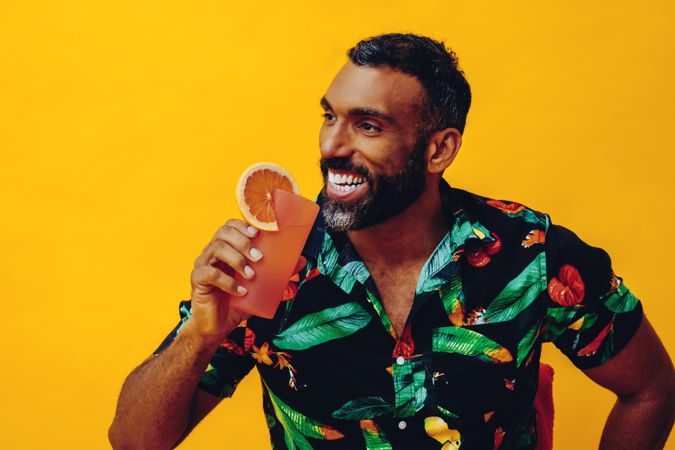Smiling Black male sitting down and drinking a cocktail in yellow room, copy space