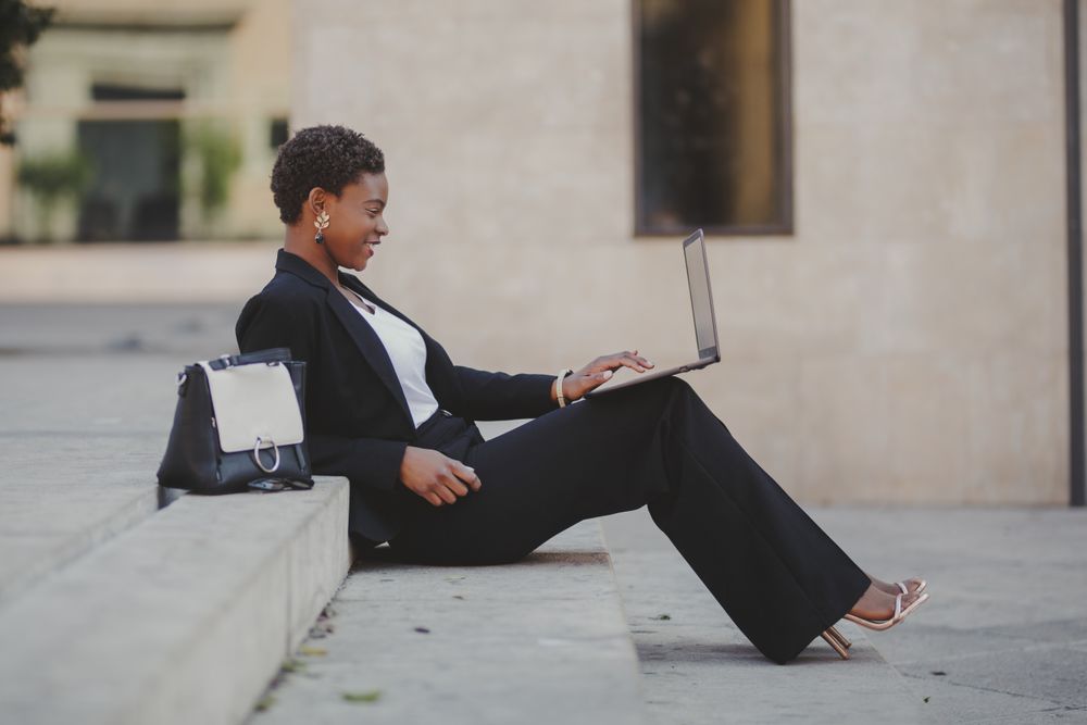 Stylish Black woman with laptop on steps near handbag