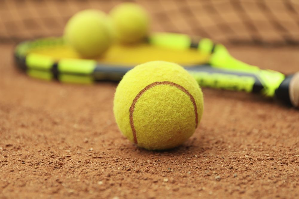Tennis racquet with tennis balls on clay court