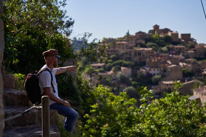 Traveling man sitting on fence and pointing at old town