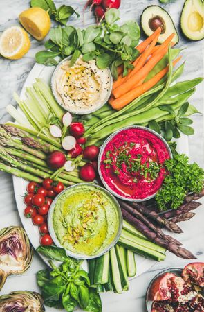 Top view of fresh colorful vegetables and dips with hummus, avocados, asparagus, carrots on plate