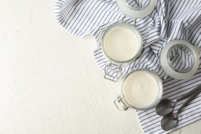 Glass jars with sour cream yogurt, spoons and towel on cement background