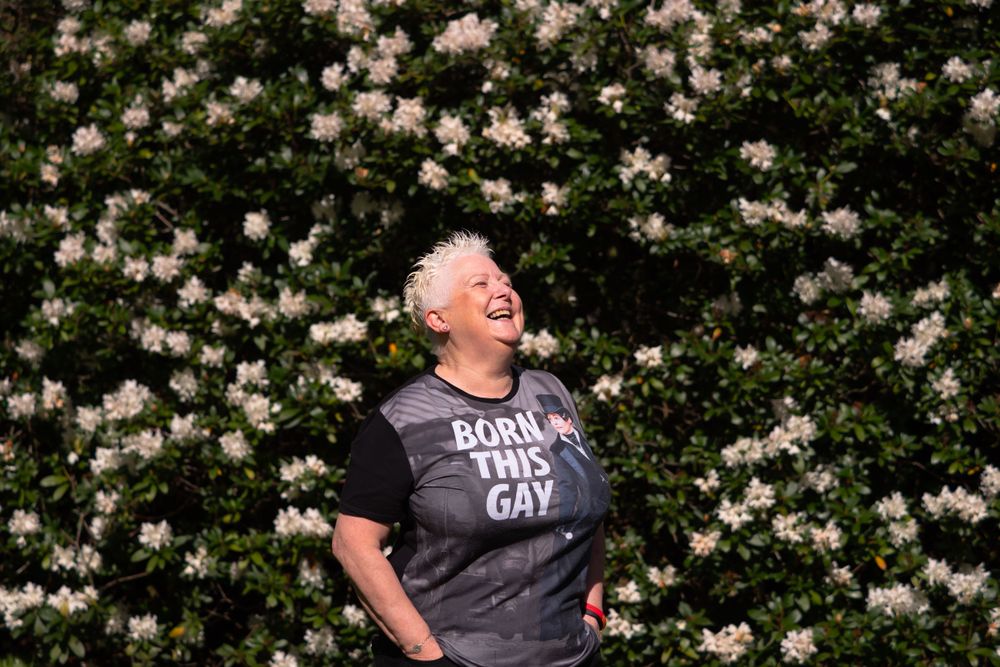 Woman with spiky grey hair smiling in front of green hedge