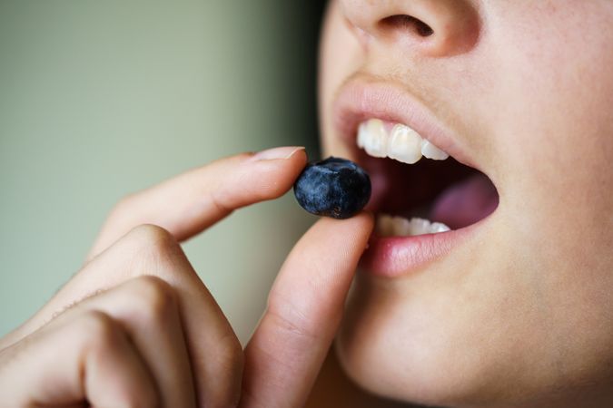 Teenager with mouth open eating fresh blueberries
