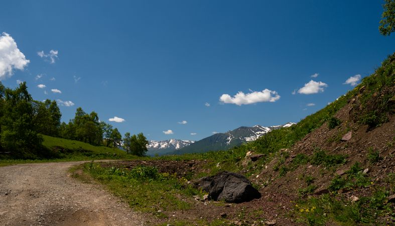 Dirt path winding through green hills with mountains in background.
