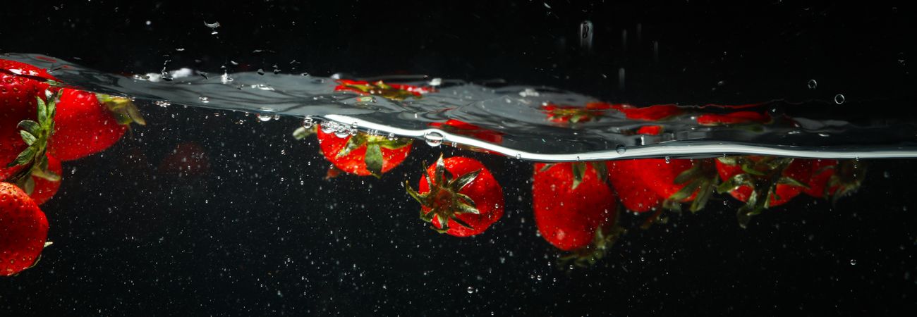 Side view banner of wave of water on dark background with floating strawberries