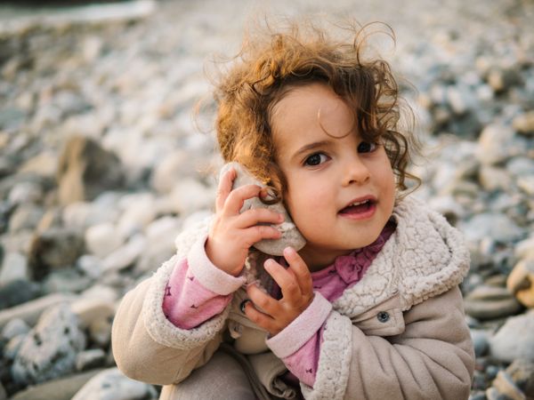 Toddler girl playing with seashell on beach