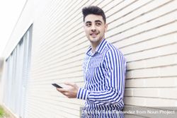 Side view of man leaning on house wall while checking his smartphone 5kROrQ