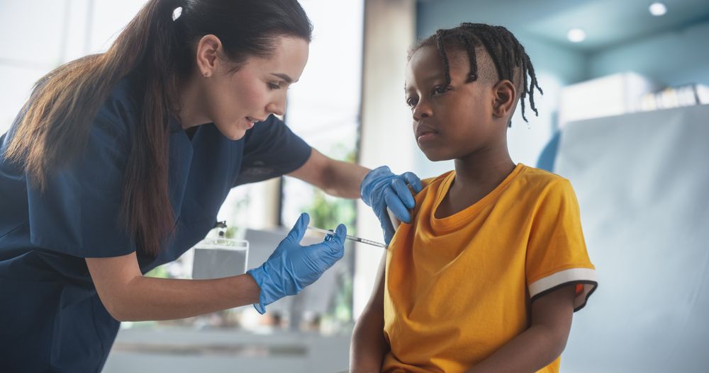 Female Nurse Is Performing Injection. Professional Woman Talks To Worried Kid, Calms Him Down.