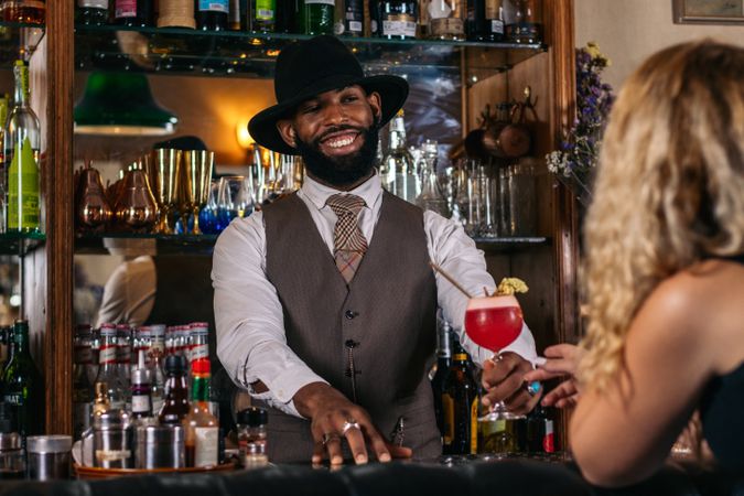 stylish Black bartender offering a customer a cocktail decorated with garnish in a traditional cocktail bar