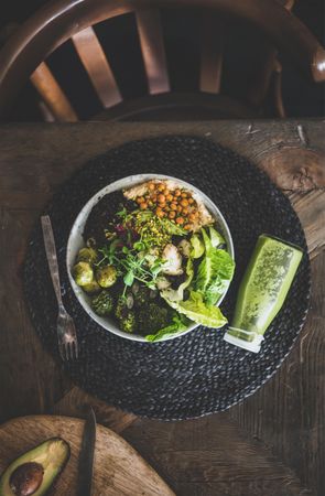 Healthy vegetarian bowl with smoothie, on table with dark chair, placemat, copy space