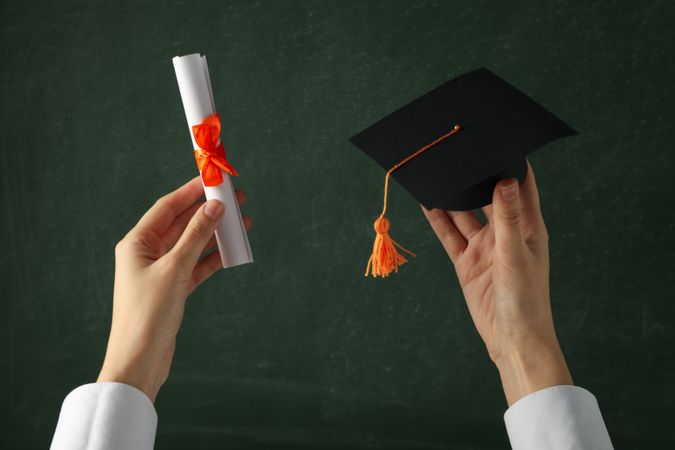 Miniature graduate hat and diploma, in hands.