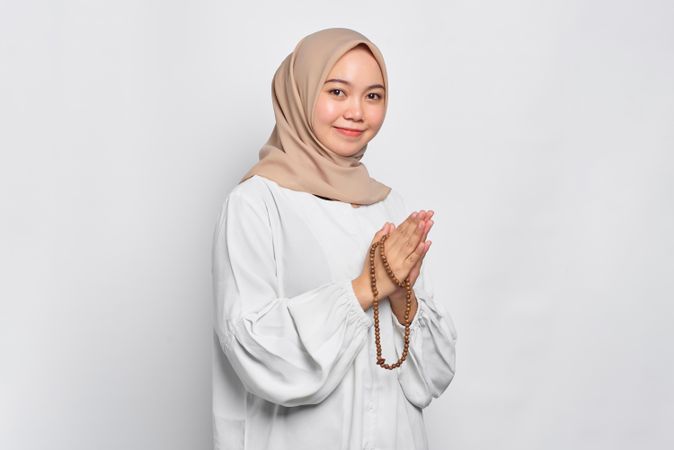 Happy Muslim woman in headscarf and light blouse with hands together with prayer beads