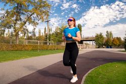 Woman jogs in park, wearing blue top and sunglasses