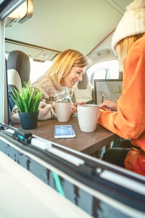 Female friends working remotely in back of van while camping, vertical