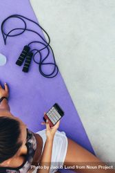 Top view of young woman sitting on exercise mat using fitness app on her mobile phone bezYN0
