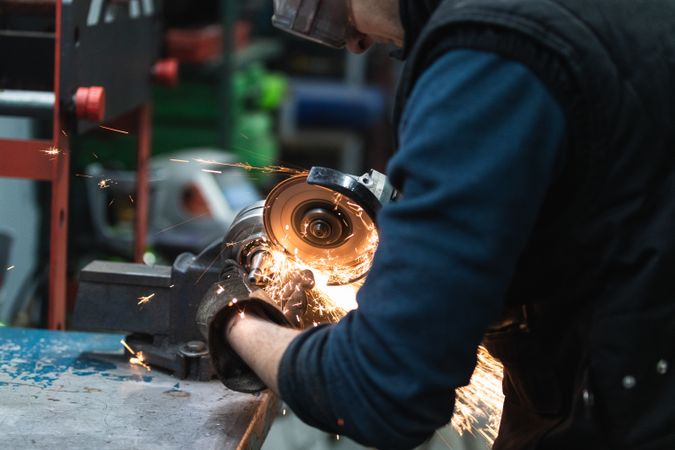 Attentive repairman cutting metal with electric grinder in workshop