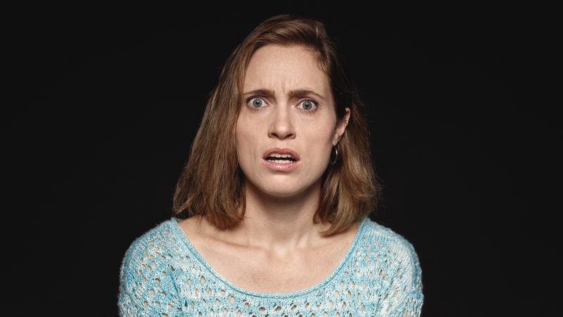 Close up of woman with short brown hair looking at camera with an expression of shock