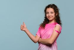 Smiling girl giving thumbs up after vaccination.