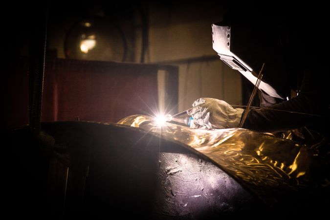 Man in mask welding metal ware in darkness