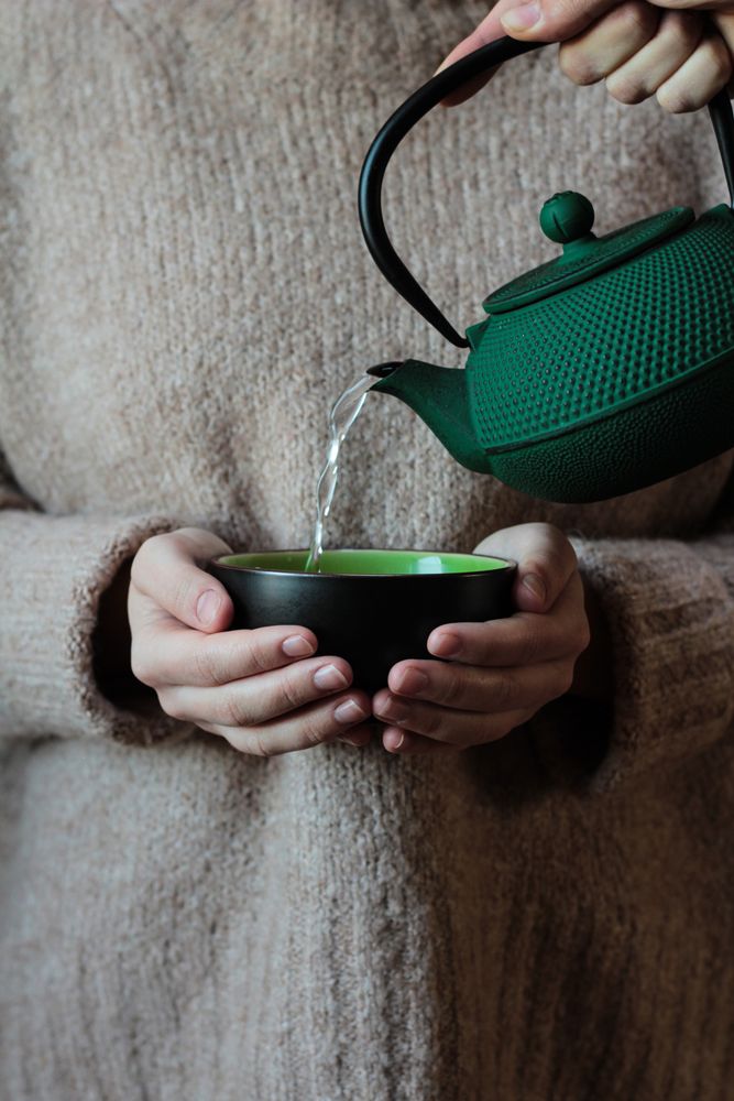 Person pouring tea to cup in hands of woman