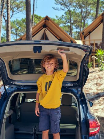 Boy standing in car trunk and looking at camera