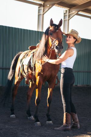 Woman taking care of his brown horse in an equestrian center