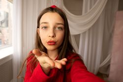 Teen girl blowing kiss toward camera in selfie photo.