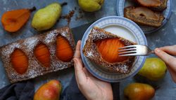 Person with pear cake on dish and fruits on table