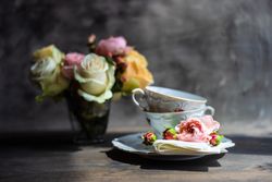 Side view of tea cups with roses in vase in background