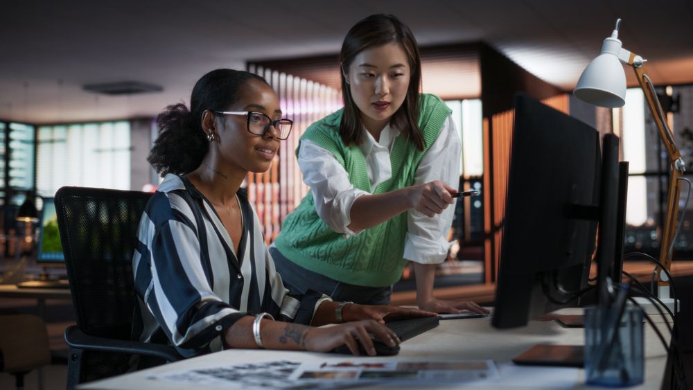 Asian Female Creative Director Giving Instructions on 3D Visuals to Black Female VFX Animator in Creative Agency Modern Office.