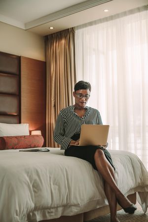Woman sitting on bed in hotel room using laptop