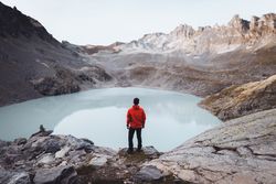 Back view of a hiker standing on waterside of frozen lake during daytime 0JJan0