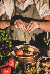 Woman in gray apron putting herbs on stew