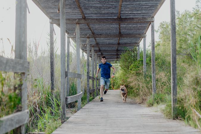 Happy adult man running with dog along countryside