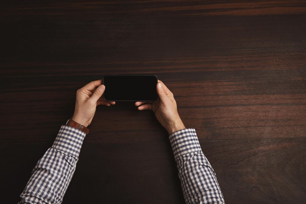 Arms in plaid shirt and leather watch strap holding cell phone horizontally