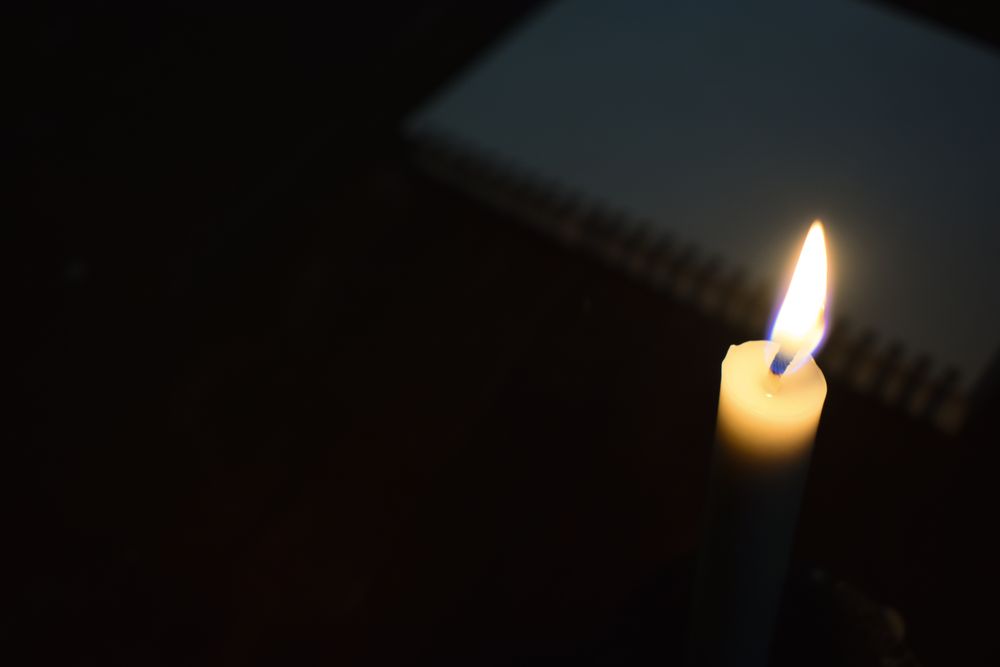 Top view of candle lit in the dark with copy space and notebook in background