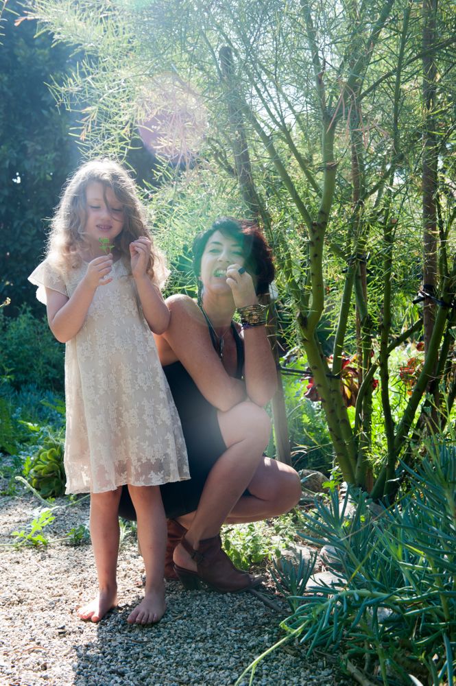 Mother and daughter snack on edible plants in garden with sun rays