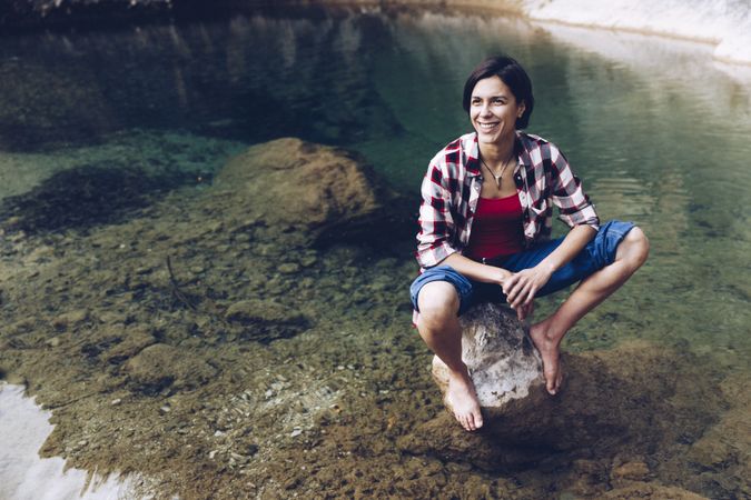 Cheerful woman sitting on rock in clear water