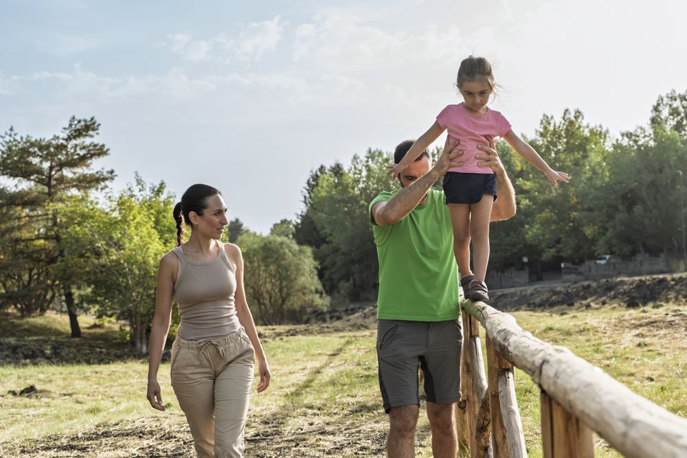 Father lifting daughter during nature walk with mom on sunny countryside trail